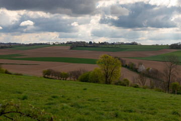 Fototapeta na wymiar A dramatic cloudscape above the rolling hills in the South of Limburg in the Netherlands. The colourful landscape is split by winding roads and small paths.