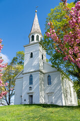 Fototapeta na wymiar Warwick, NY-USA-May 1, 2021: Vertical view of the historic Old School Baptist Meeting house flanked by flowering trees located in center of the village of Warwick.