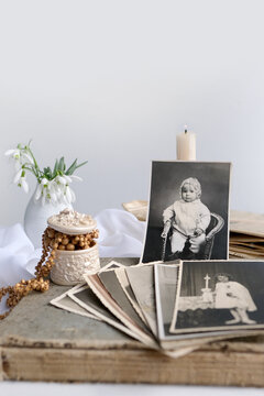 stack of vintage photos, pictures of children of first communion of 1950, candle is lit, spring flowers in vase, concept of family tree, genealogy, childhood memories