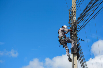 An electrician climbing wearing equipment safety harness an electric pole to install the wires....