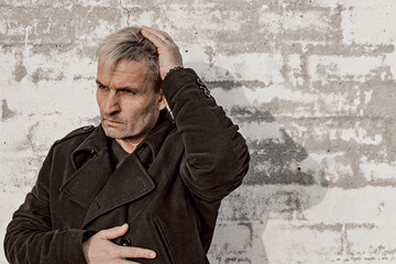 Middle aged blonde man in trendy clothes is posing in front of a white brick wall. Male fashion photoshoot. Men's mental health. Emotions. Front view, copy space.