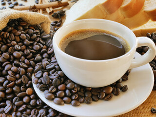 A cup of aroma coffee and a sack of coffee beans with some bread for drink and eat in the breakfast