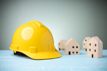 Yellow hard hat with many mini wood houses on blue wooden table with copy space and green background. Concept construction home, and safety on work. Personal protective equipment.