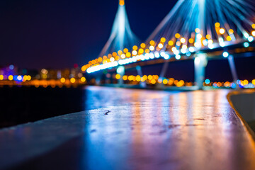 Suspension bridge over the river. Highlighting the bridge. Panorama of the night city. Close up view from the level of the fence.