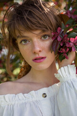 Fototapeta premium A young woman with blossom cherry near face, close-up portrait