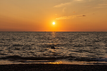 Obraz premium Beautiful orange sunrise is on the beach by the sea with black ship silhouettes and a group of swimming people