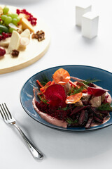 Beet summer salad with arugula, radicchio, soft cheese and walnuts on plate dressing and spices on blue plate, copy space, top view