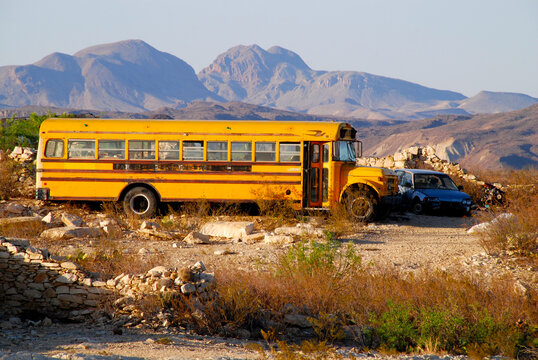 typical old yellow school bus parked in the desert next to a junk car