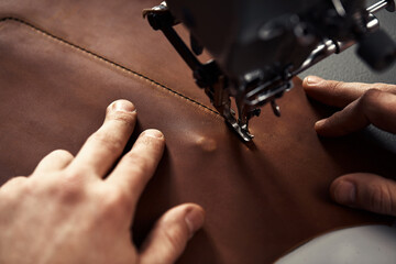 Working process of leather craftsman. Tanner or skinner sews leather on a special sewing machine,...