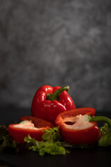 Rote Paprika liegt auf den Salatblättern, auf dem schwarzen Hintergrund. Eine Paprika ist durchgeschnitten, die zweite ist im Stück. Hochformat, oben ist viel Platz zum beschriften.
