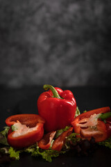 Rote Paprika liegt auf den Salatblättern, auf dem schwarzen Hintergrund. Eine Paprika ist durchgeschnitten, die zweite ist im Stück. Hochformat, oben ist viel Platz zum beschriften.