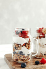 A healthy, dietary breakfast or snack of granola or oatmeal muesli with yoghurt and fresh wild berries. Light background and vertical photo. Copy space