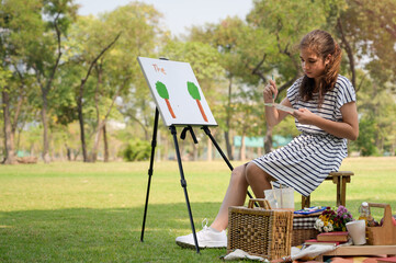 A half-Thai-European girl  is sitting on the wooden bench and painted on the canvas placed on a drawing stand