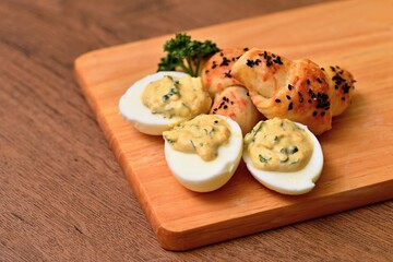 Eggs mimosa cheese mini-croissant on a wooden board. Arranged eggs and pastries with a sprig of curly parsley. Eggs stuffed with cream, homemade pastries rolls on a wooden background.
