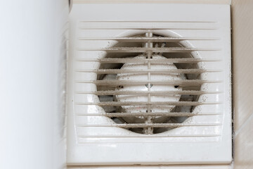 Dirty air vent with electric fan on the wall inside the room.