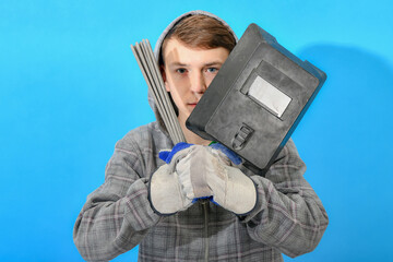 Young welder with electrodes and welding shield on a blue background.