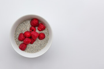 Chia pudding  with raspberries in white round bowl on white background