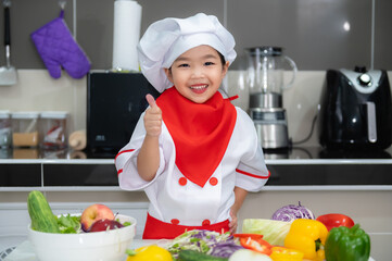 Cute asian girl wear chef uniform with a lot of vegatable on the table in the kitchen room,Make food for eat dinner,Funny time for kids