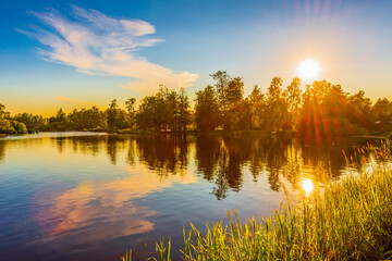 River passing through the village. Sunset over the forest. Blue sky. Beautiful nature. Summer evening. View from the grassy shore.