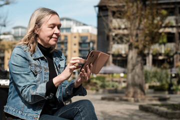 Mature blonde woman using her smartphone sitting on a bench.