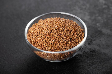 buckwheat in glass bowl, cereals  on a black background, horizontally