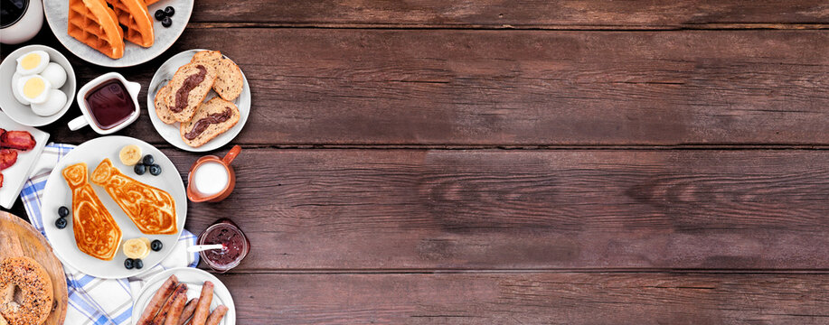 Fathers Day breakfast side border. Overhead view on a dark wood banner background. Tie pancakes, mustache toast and a selection of dad themed food.