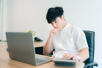 Portrait of young professional asian businessman with white shirt serious and concentration thinking for analyze, deep focus to create idea while use computer laptop at home office ,new normal concept