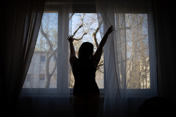 Fototapeta na wymiar Silhouette of a girl in front of a window lit by morning light