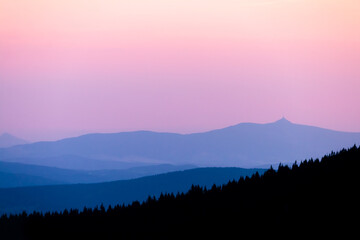 Colorful sunset in Czech mountains. Blue mountain ranges layers against pink to orange evening sky in the Krkonose national park.