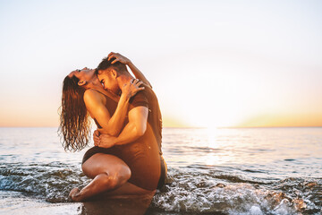 Happy young fit couple embrace each other with love in the sea or ocean at summer sunset. Romantic...