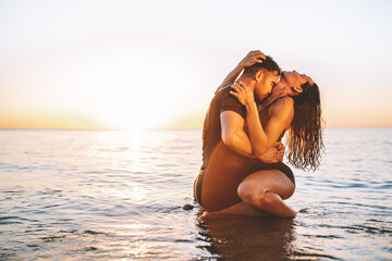 Happy young fit couple embrace each other with love in the sea or ocean at summer sunset. Romantic mood, tenderness, relationship, vacation concept.