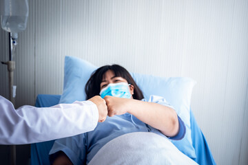Doctor and patient which wearing a surgical mask, use hands fist bump to encouragement, cooperation  team In process of successful treatment, picture focuses on the hand, to health care concept