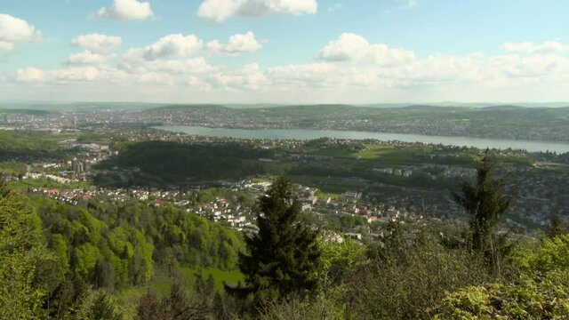 Panning Zurich, The Surrounding Area, And Zurichsee Lake From High Atop A Hill, With Bright Blue Sky, Clouds, Trees, And Rolling Hills Stretching To The Horizon