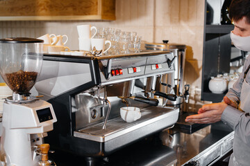 A masked barista prepares delicious coffee at the bar in a cafe. The work of restaurants and cafes during the pandemic.
