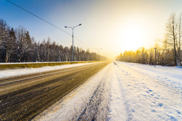 Sunrise on a clear winter morning, empty highways in snow. View from the side of the road. Coniferous forest. Russia, Europe. Beautiful nature.