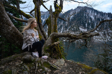 Girl sits on a tree and meditates on blue lake background. Lake Ritsa in Abkhazia