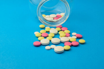 Colored pills scattered from a glass jar, on a blue background, close-up. The concept of medicine and treatment for coronavirus. Copy space. Focus on the foreground.
