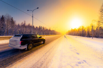 Fototapeta premium Sunrise on a clear winter morning, the car rides on the highways in the snow. View from the side of the road. Coniferous forest. Russia, Europe. Beautiful nature.