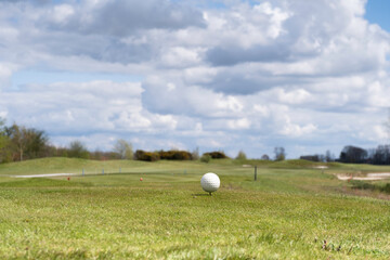 White golf ball on a tee in a golf course with beautiful cloudy sky above.
Focus on the golf ball, shallow depth of field