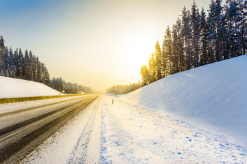 Fototapeta premium Sunrise on a clear winter morning, empty highways in snow. View from the side of the road. Coniferous forest. Russia, Europe. Beautiful nature.