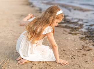 Little girl sitting on the sandy beach near the sea.