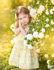Sad and funny little girl in spring garden. Angry child in the park.