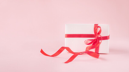 White gift box with red ribbon bow on pink background with copy space.