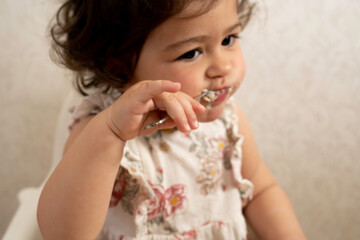 spoon in a child's hand, caucasian beautiful girl in the background with a spoon in her mouth out of focus