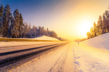 Fototapeta na wymiar Sunrise on a clear winter morning, empty highways in snow. View from the side of the road. Coniferous forest. Russia, Europe. Beautiful nature.