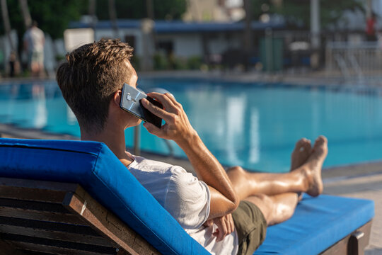 millennial man using the phone on the poolside. picture from the back