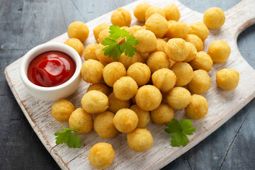 Crispy potato balls with ketchup on white wooden board