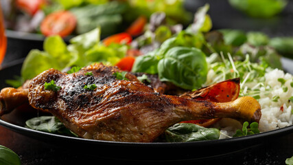 Slow cooked aromatic duck legs with basmati rice and side salad served with orange wedges on black plate