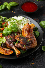 Slow cooked aromatic duck legs with basmati rice and side salad served with orange wedges on black plate