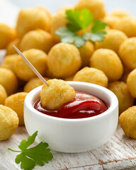 Crispy potato balls with ketchup on white wooden board